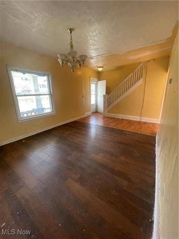 empty room featuring a notable chandelier, dark hardwood / wood-style floors, and a textured ceiling