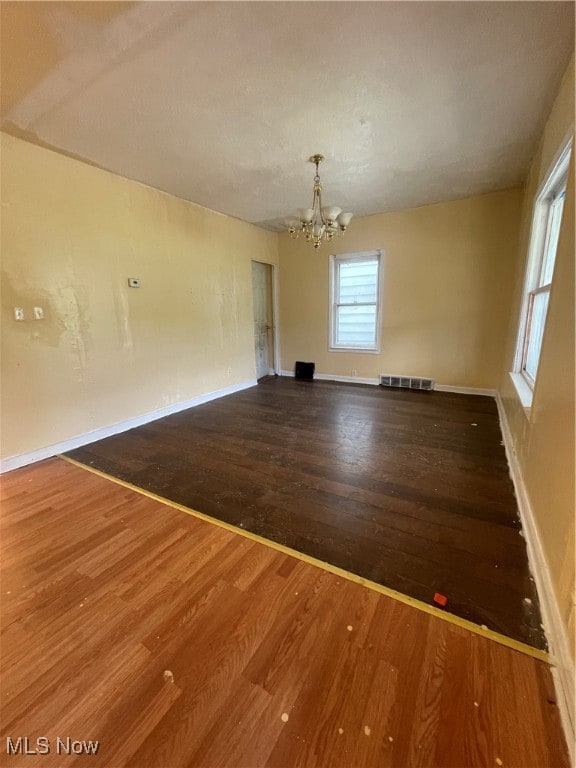 spare room with a chandelier and wood-type flooring