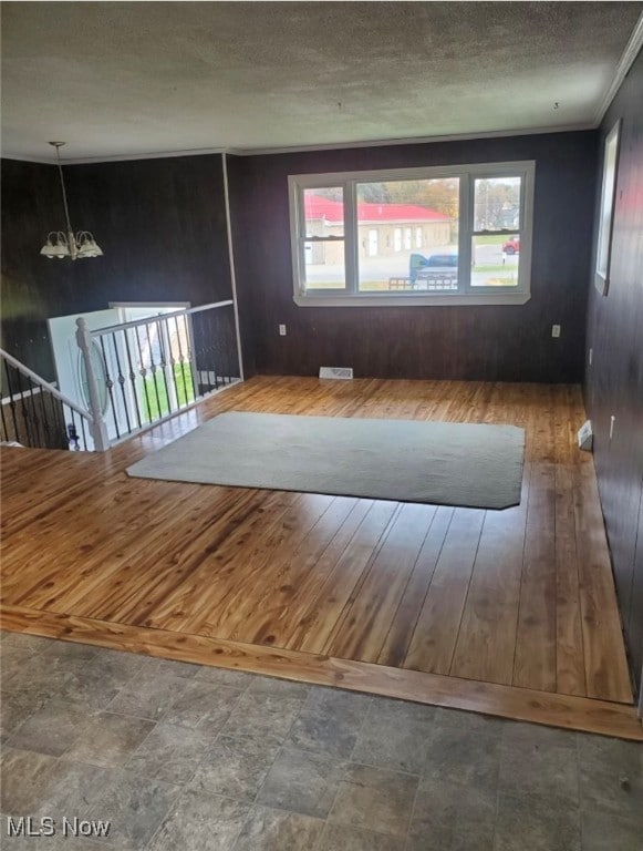 empty room featuring a textured ceiling, a notable chandelier, hardwood / wood-style flooring, and a healthy amount of sunlight