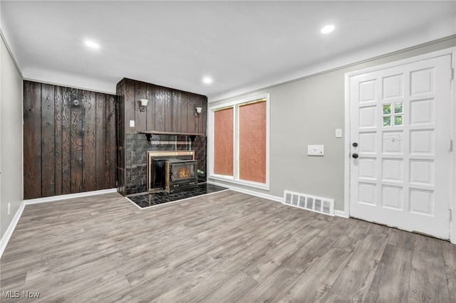 unfurnished living room with a fireplace, wooden walls, and light wood-type flooring