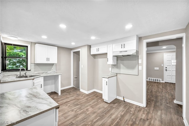 kitchen with light stone counters, sink, tasteful backsplash, wood-type flooring, and white cabinetry