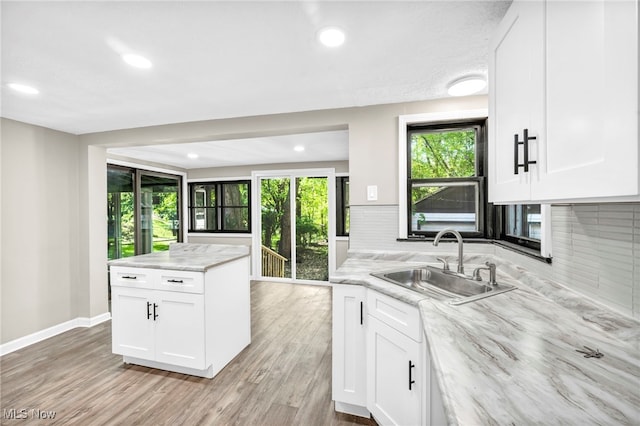 kitchen featuring light stone counters, white cabinetry, sink, and backsplash