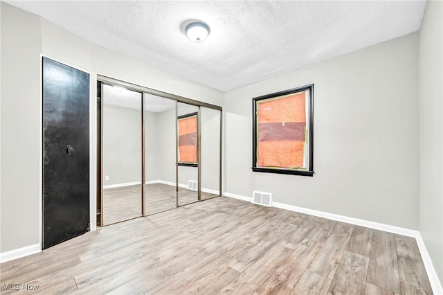 unfurnished bedroom featuring light wood-type flooring, a closet, and a textured ceiling