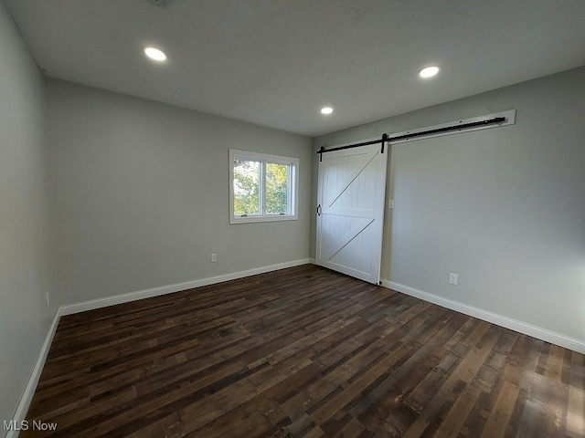 unfurnished bedroom featuring a barn door and dark hardwood / wood-style flooring