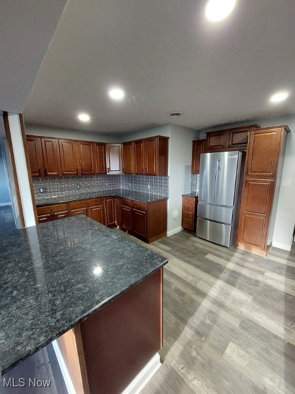 kitchen featuring light hardwood / wood-style floors, stainless steel fridge, tasteful backsplash, dark stone counters, and kitchen peninsula