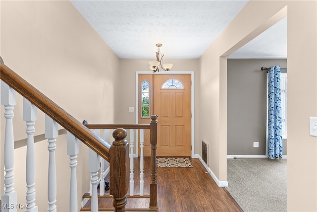 foyer entrance featuring a textured ceiling, an inviting chandelier, and dark hardwood / wood-style flooring