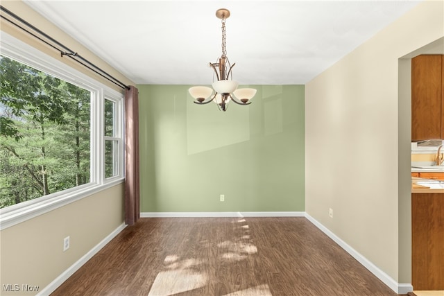 unfurnished dining area with dark wood-type flooring and an inviting chandelier