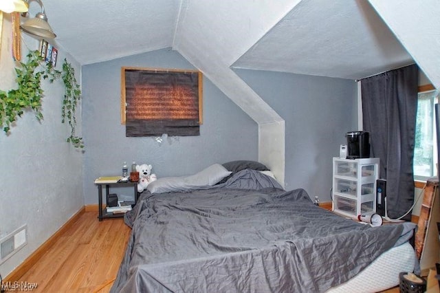 bedroom with lofted ceiling, wood-type flooring, and a textured ceiling