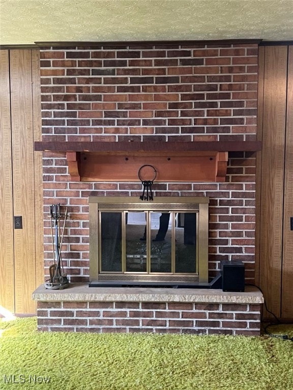 interior details with wood walls, a brick fireplace, and a textured ceiling