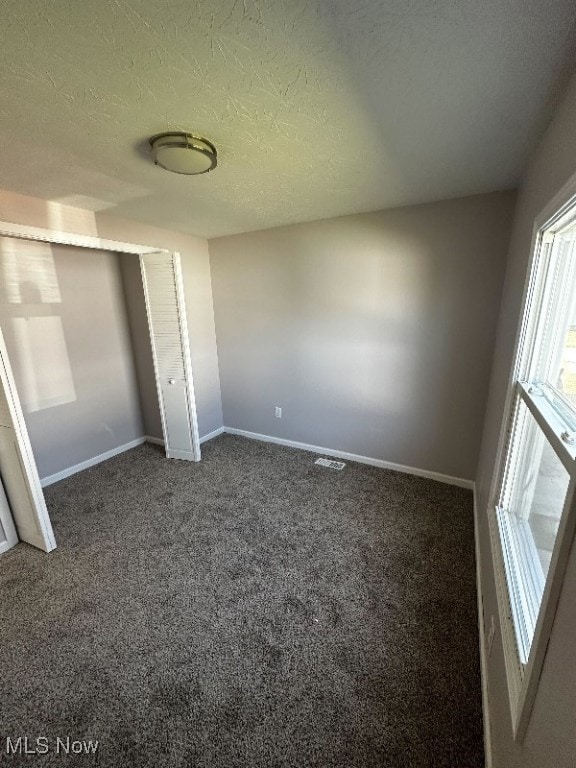 unfurnished bedroom featuring a closet, dark carpet, and a textured ceiling