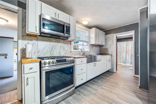 kitchen with light wood-type flooring, sink, butcher block counters, appliances with stainless steel finishes, and white cabinetry