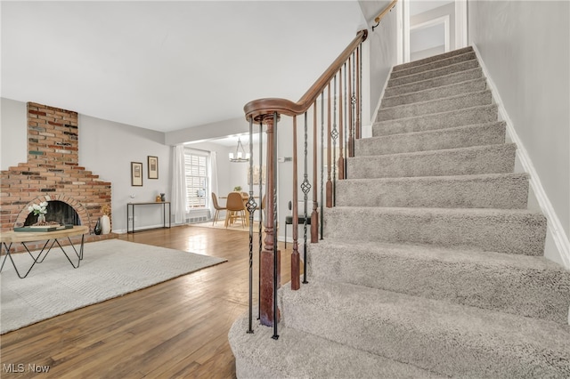 staircase with hardwood / wood-style floors and a brick fireplace