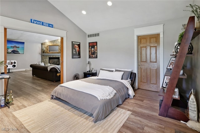 bedroom with a fireplace, light hardwood / wood-style floors, and lofted ceiling