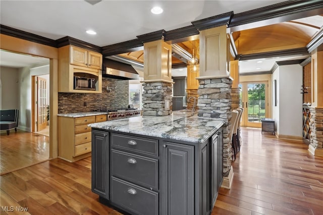 kitchen featuring light stone counters, crown molding, exhaust hood, an island with sink, and hardwood / wood-style flooring