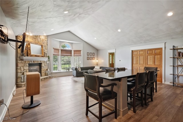 dining room with a stone fireplace, wood-type flooring, and lofted ceiling