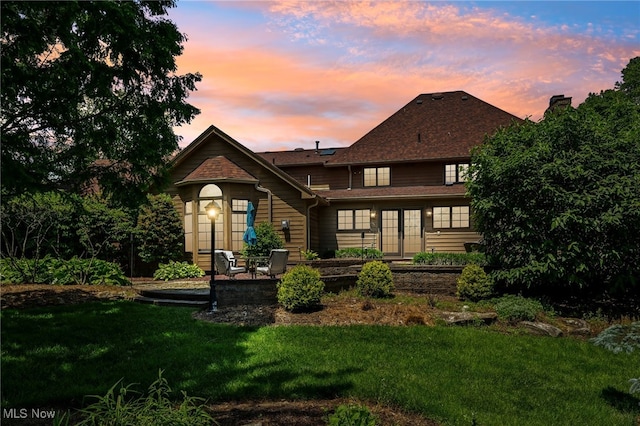 back house at dusk with a patio area and a yard