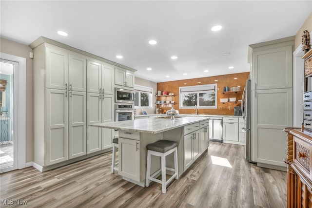 kitchen featuring light wood-type flooring, a kitchen island, a kitchen breakfast bar, light stone counters, and appliances with stainless steel finishes