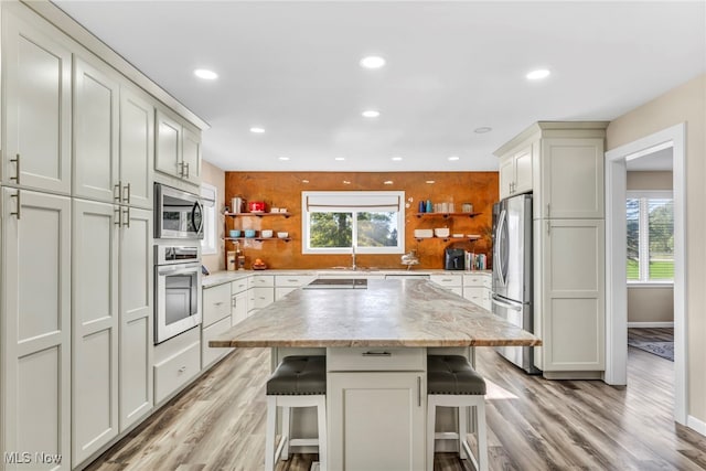 kitchen with light hardwood / wood-style flooring, appliances with stainless steel finishes, a healthy amount of sunlight, and a breakfast bar