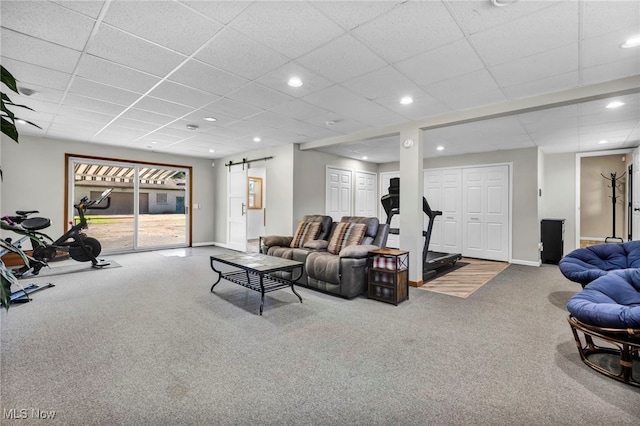 carpeted living room featuring a barn door and a drop ceiling