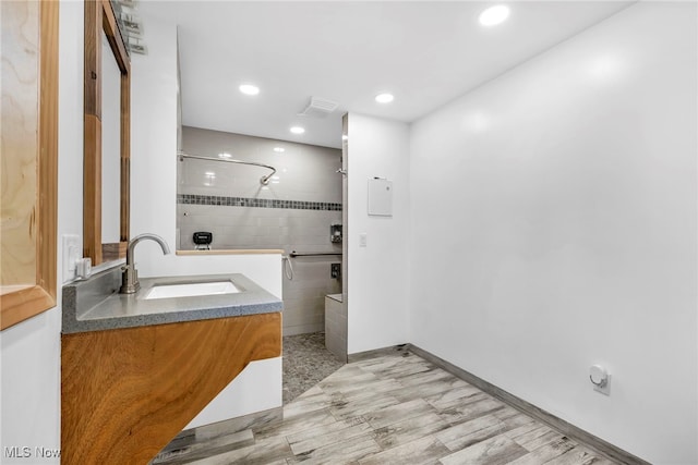 bathroom with a tile shower, hardwood / wood-style flooring, and vanity