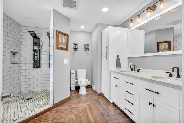 bathroom featuring parquet flooring, vanity, tiled shower, and toilet