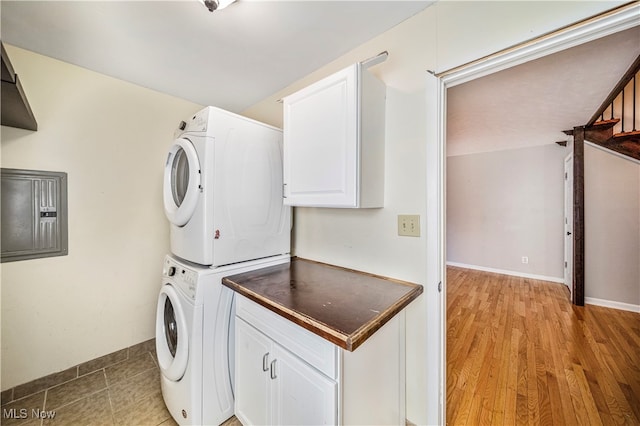 laundry room featuring stacked washer / drying machine, electric panel, light wood-type flooring, and cabinets