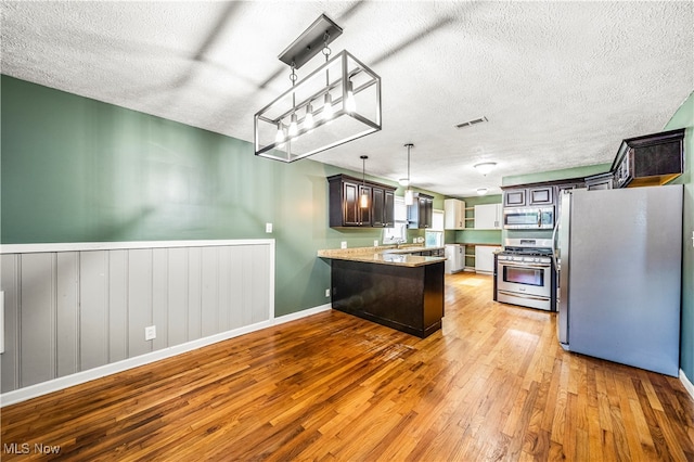 kitchen featuring appliances with stainless steel finishes, a textured ceiling, pendant lighting, light hardwood / wood-style floors, and dark brown cabinetry