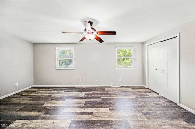 unfurnished bedroom featuring dark wood-type flooring, ceiling fan, a closet, and multiple windows