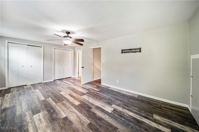 unfurnished bedroom featuring dark hardwood / wood-style floors, multiple closets, and ceiling fan