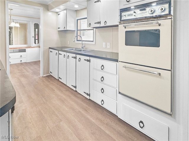 kitchen with white cabinets, oven, light wood-type flooring, and sink