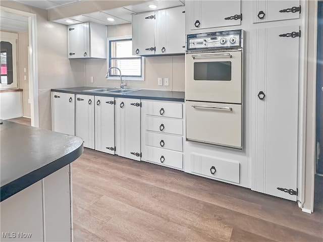 kitchen with sink, white cabinetry, white oven, and light hardwood / wood-style floors