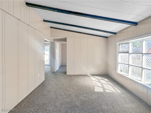 empty room featuring carpet floors, a textured ceiling, plenty of natural light, and lofted ceiling with beams