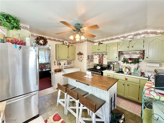 kitchen with ceiling fan, green cabinets, sink, appliances with stainless steel finishes, and a kitchen bar