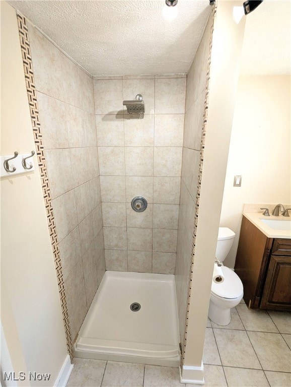 bathroom featuring tiled shower, tile patterned floors, toilet, vanity, and a textured ceiling