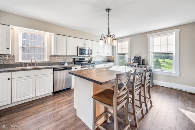 kitchen with white cabinets, sink, appliances with stainless steel finishes, a center island, and dark hardwood / wood-style flooring