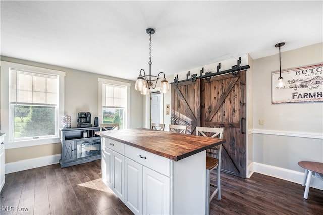 kitchen featuring wooden counters, decorative light fixtures, white cabinetry, a barn door, and dark hardwood / wood-style flooring