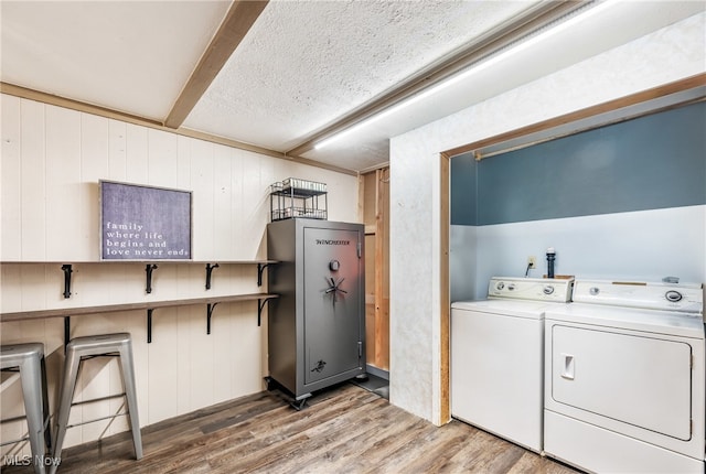 washroom featuring hardwood / wood-style flooring, wooden walls, a textured ceiling, and washing machine and dryer