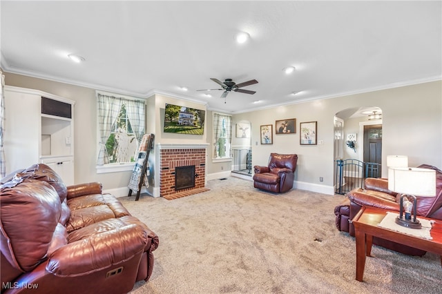 carpeted living room featuring a brick fireplace, ornamental molding, and ceiling fan