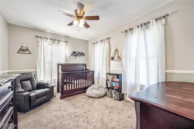 carpeted bedroom featuring a textured ceiling, a nursery area, multiple windows, and ceiling fan