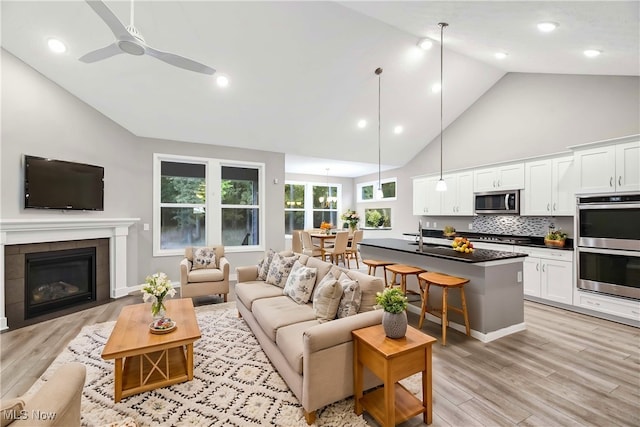 living room with ceiling fan, light wood-type flooring, a fireplace, and high vaulted ceiling