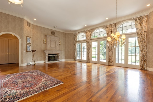 unfurnished living room featuring a notable chandelier, hardwood / wood-style flooring, crown molding, and french doors