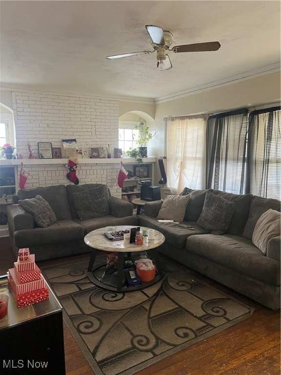 living room featuring ceiling fan, dark hardwood / wood-style flooring, ornamental molding, and brick wall