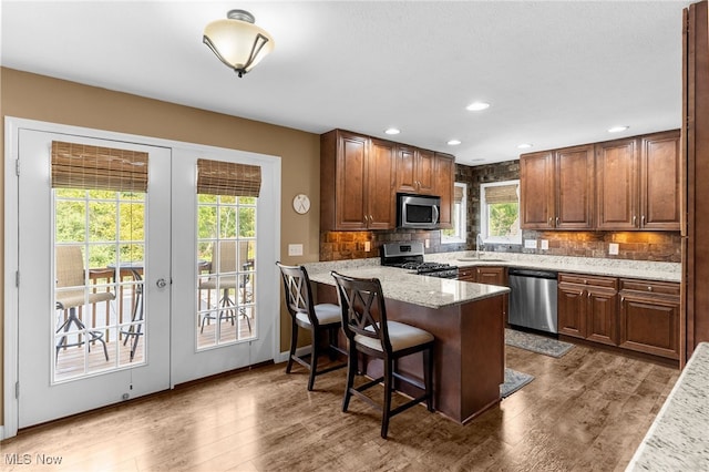 kitchen with light stone counters, wood-type flooring, kitchen peninsula, appliances with stainless steel finishes, and a kitchen breakfast bar