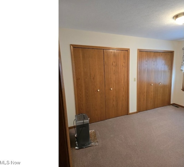 unfurnished bedroom featuring carpet flooring, a textured ceiling, and two closets