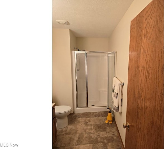 bathroom featuring vanity, toilet, a shower with door, and a textured ceiling