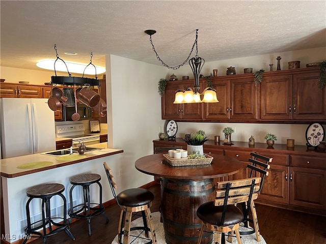 kitchen featuring a kitchen breakfast bar, dark wood-type flooring, a textured ceiling, and white appliances