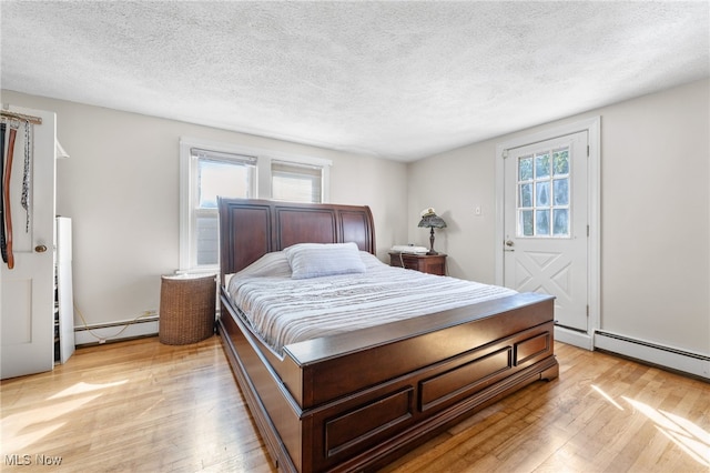 bedroom featuring light wood-type flooring, a textured ceiling, and a baseboard heating unit