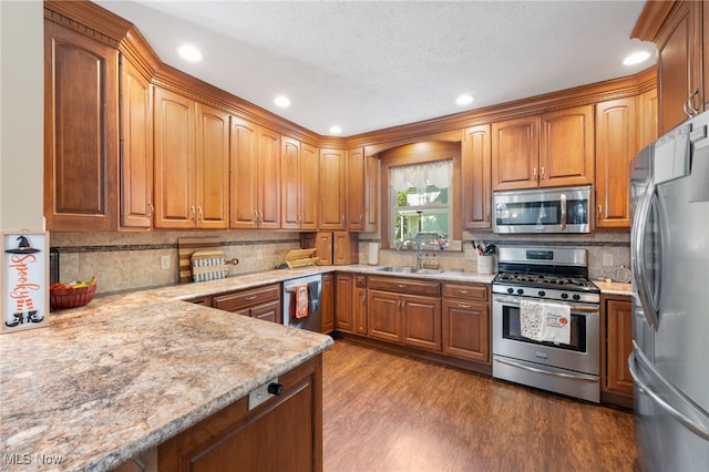 kitchen with sink, tasteful backsplash, light stone counters, appliances with stainless steel finishes, and hardwood / wood-style flooring