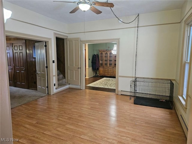 empty room with ceiling fan, light wood-type flooring, and a baseboard heating unit