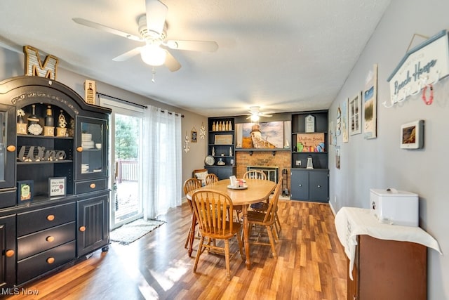 dining room with ceiling fan, a textured ceiling, a fireplace, and hardwood / wood-style floors